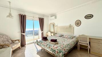 Een slaapkamer met een bed, een stoel, een dressoir, een spiegel en uitzicht op de stad.