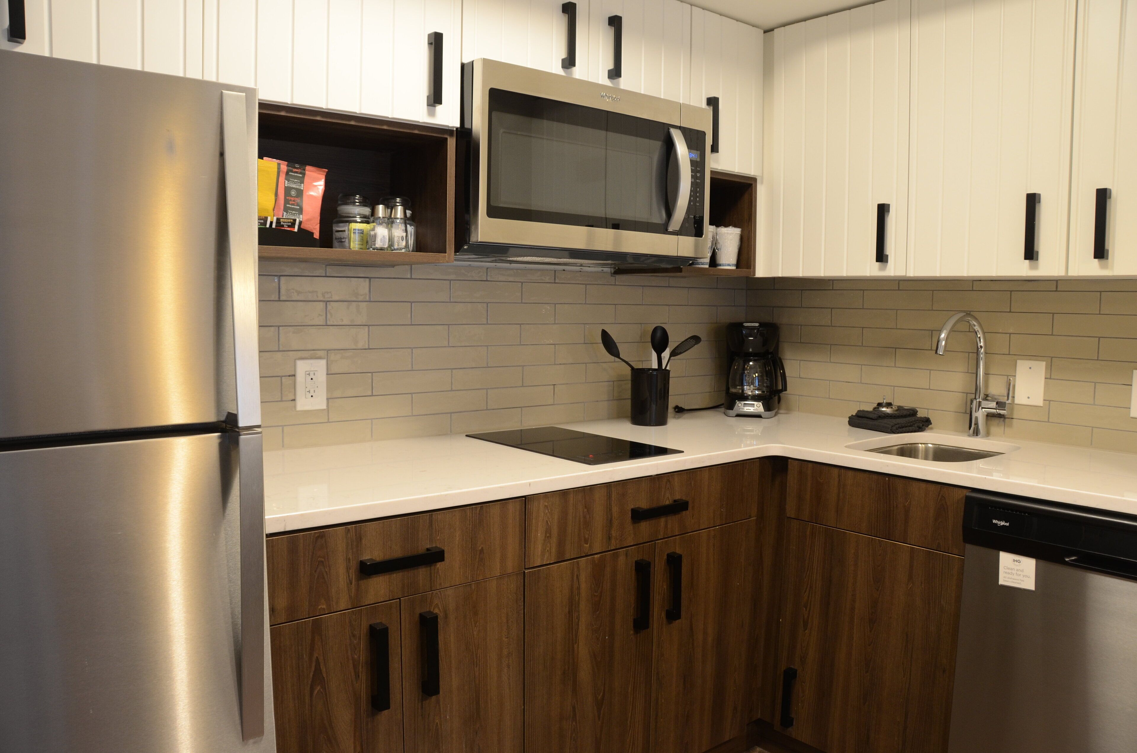 Una cocina moderna con electrodomésticos de acero inoxidable, armarios de madera y encimera blanca.