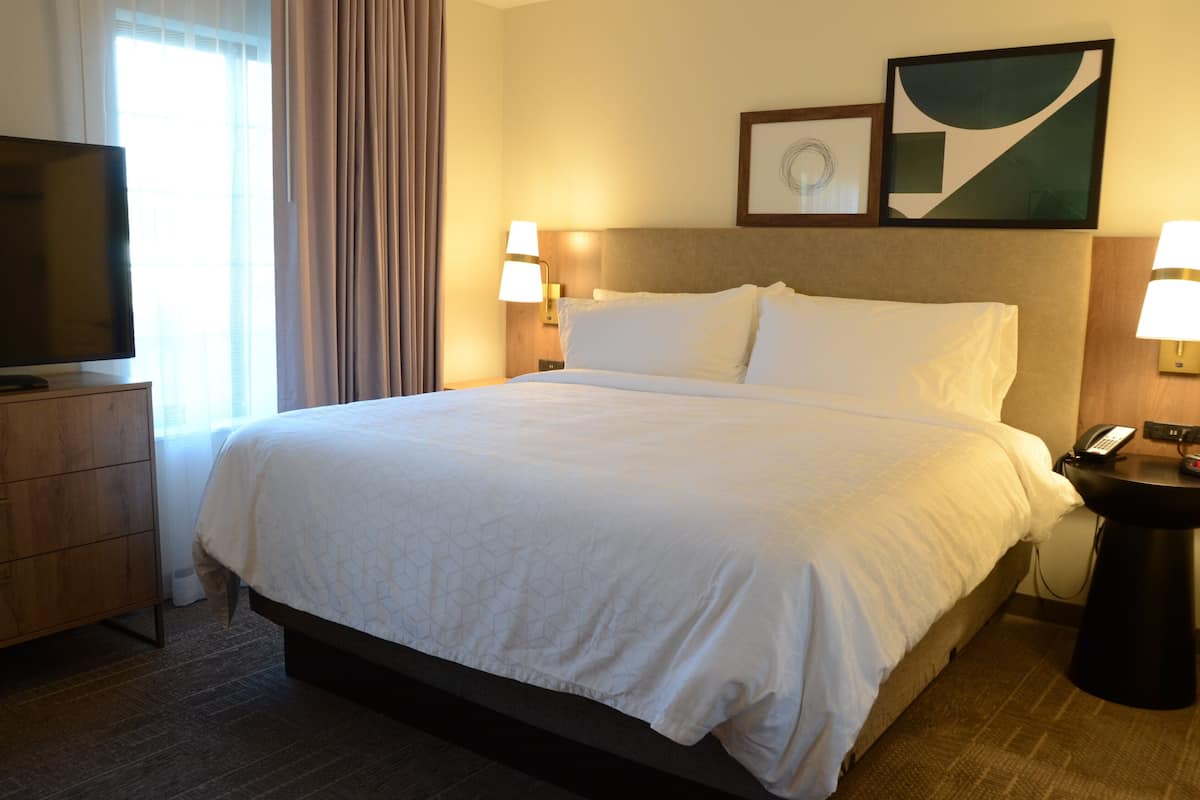 Habitación de hotel con una cama grande, dos lámparas de noche, un televisor sobre un mueble de madera y un teléfono en una mesita.