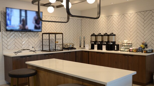 A modern kitchen with a large island, bar stools, a television mounted on the wall, and kitchen appliances. - Staybridge Suites Nashville SE - Murfreesboro by IHG (Murfreesboro)