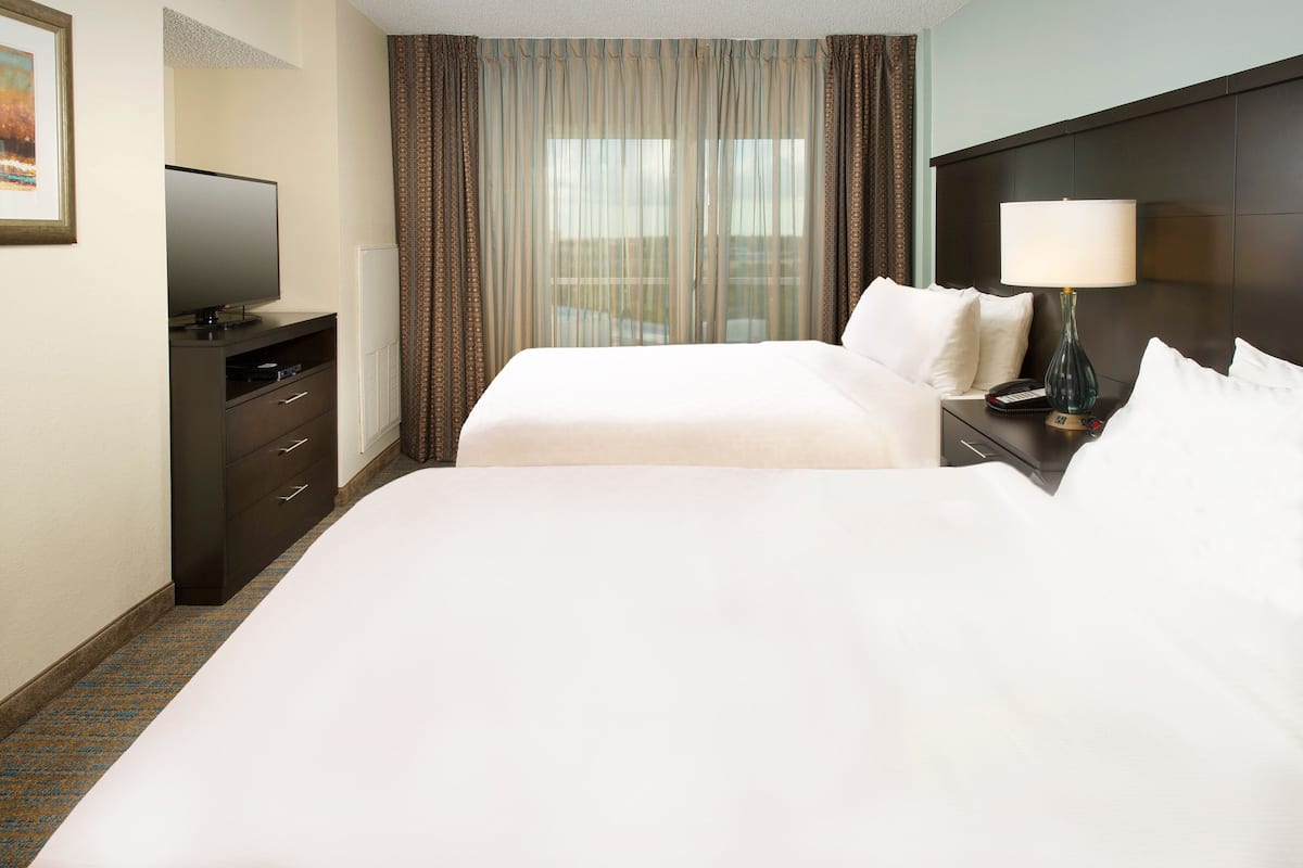 Una habitación de hotel con dos camas, un televisor, un escritorio con lámpara y una ventana con cortinas.