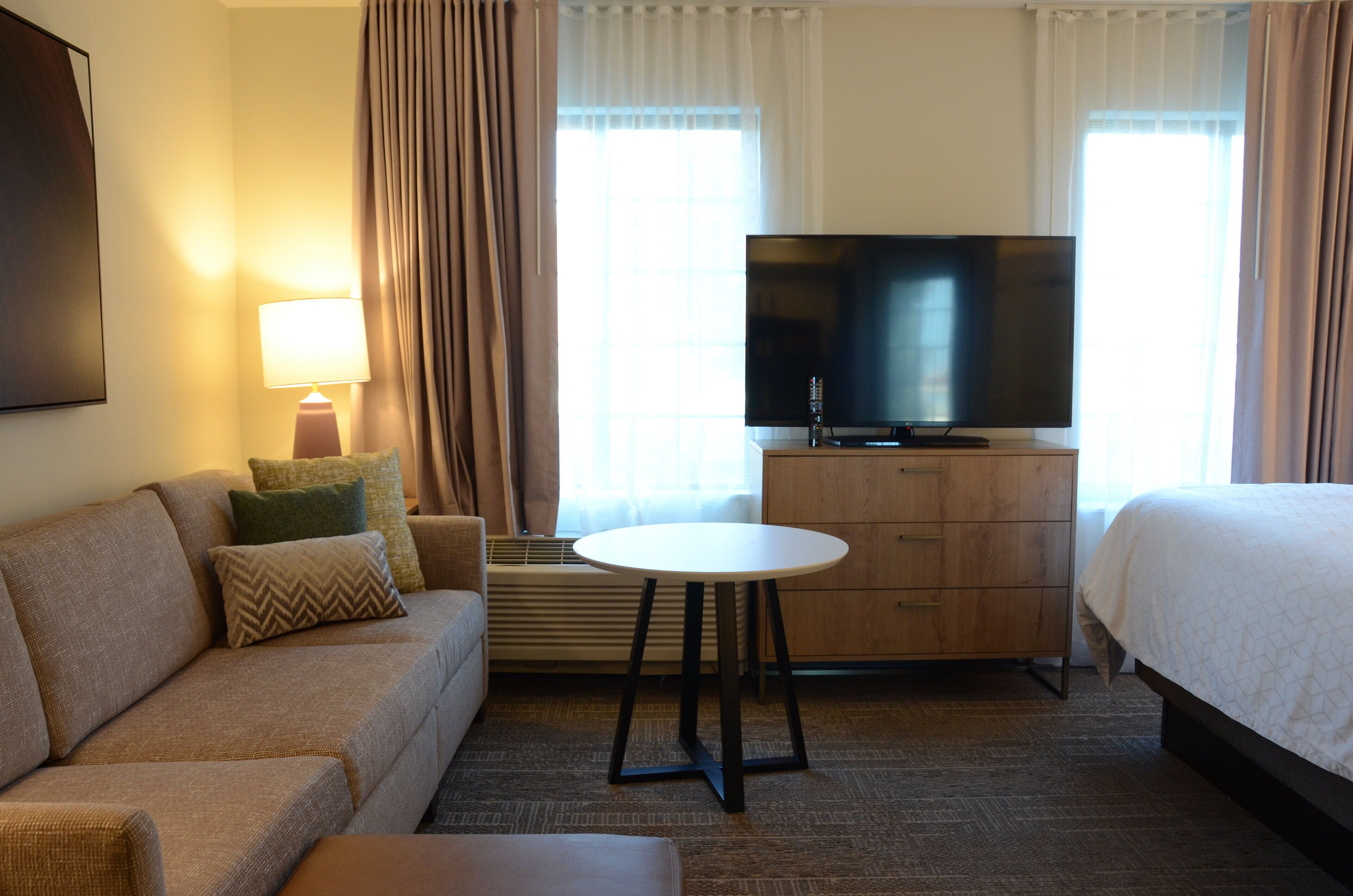 A hotel room with a sofa, a TV, a bedside table, a dresser, and a bed.