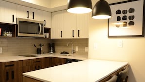 A modern kitchen with white cabinets, a microwave, a sink, and a dining area with chairs. - Staybridge Suites Nashville SE - Murfreesboro by IHG (Murfreesboro)