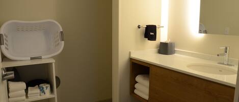 A bathroom with a white sink, wooden vanity, a mirror, a towel rack, and a shelf with towels and toiletries.