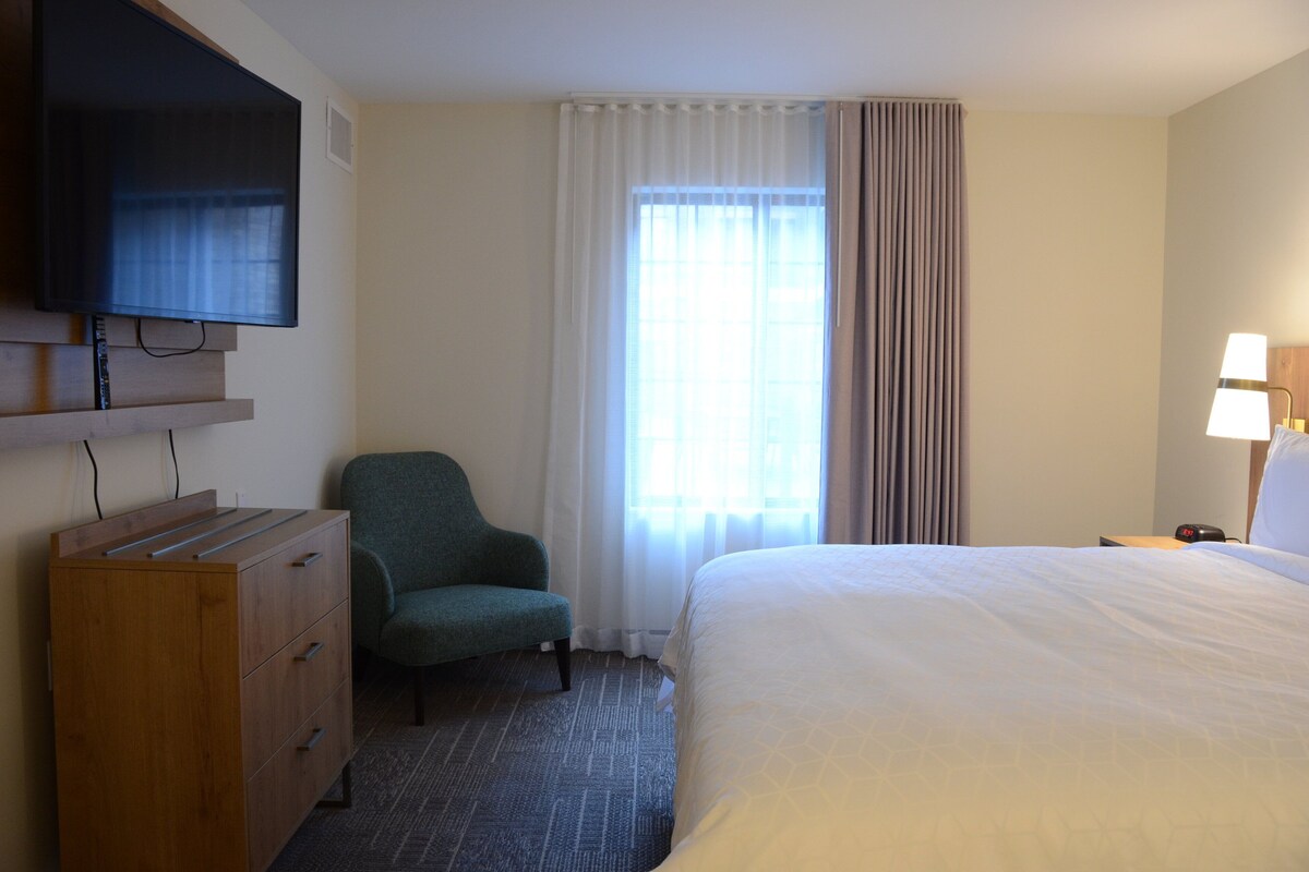 Habitación de hotel con cama, televisión montada en la pared, escritorio con lámpara y una silla.