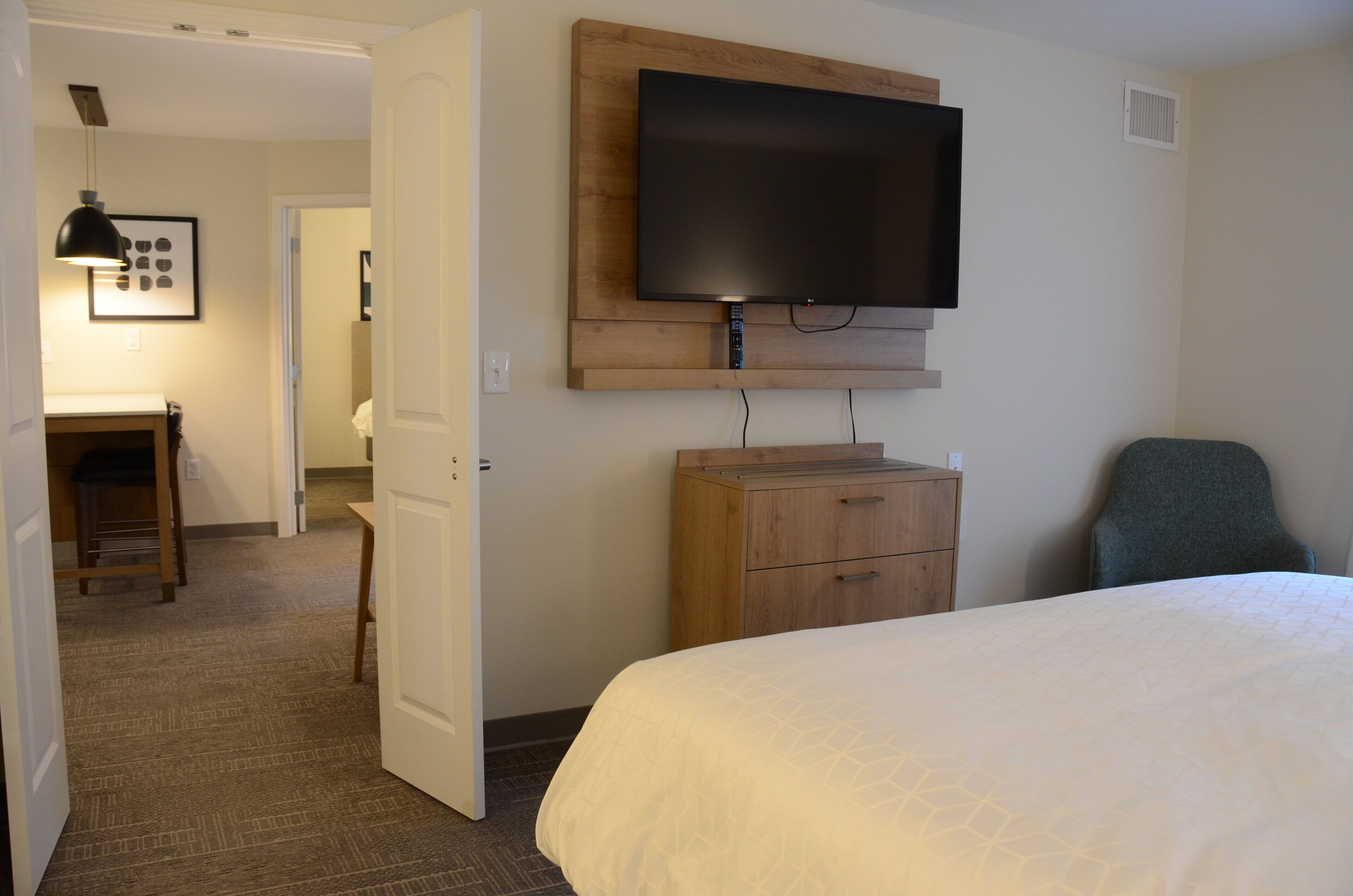 A hotel room with a large bed, a wooden dresser, a flat-screen TV mounted on the wall, and a chair.