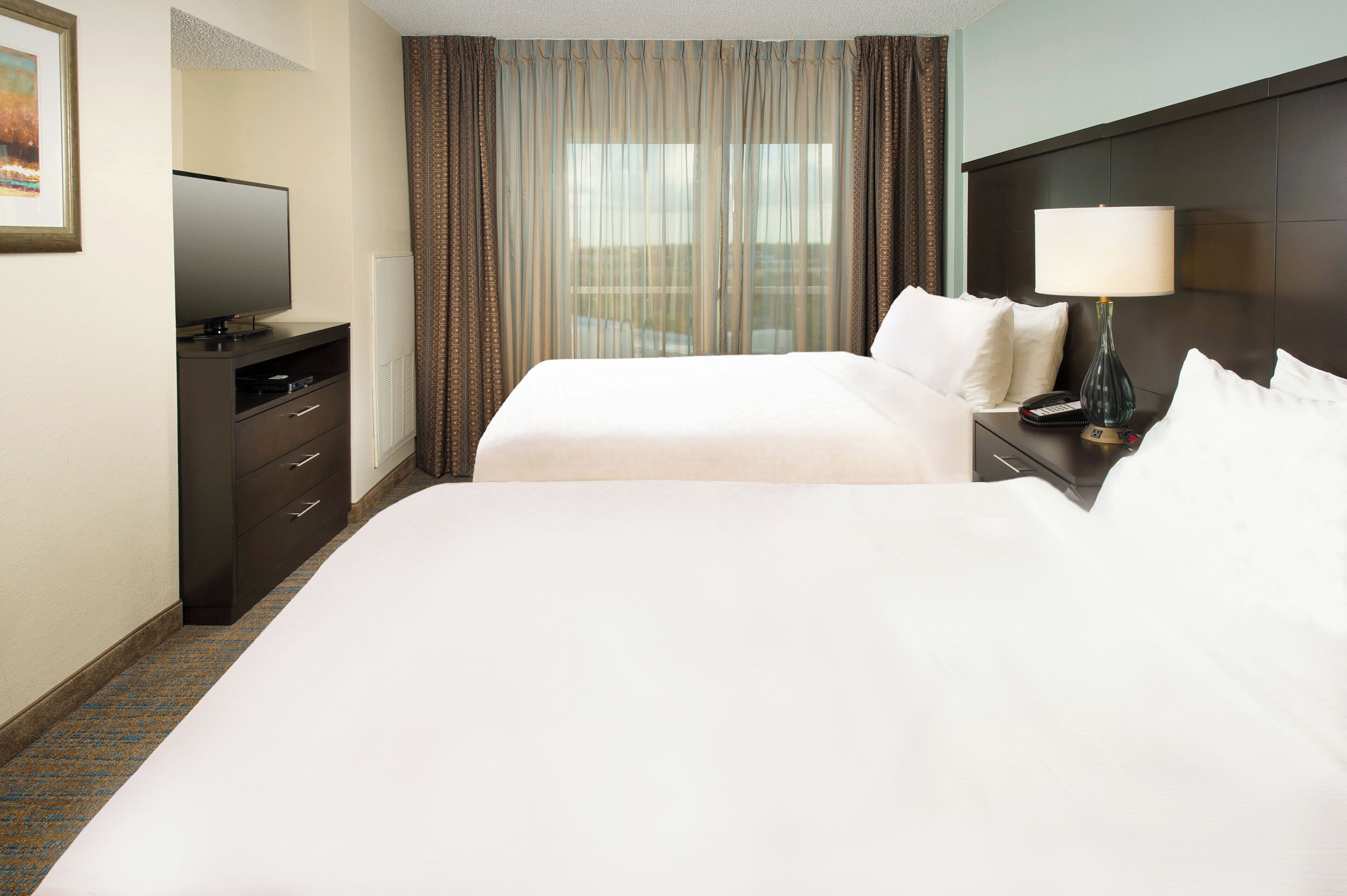 A hotel room with two beds, a desk, a television, and a window with curtains.