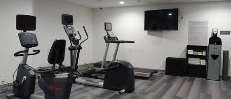 Un gimnasio con máquinas de cardio, un televisor y un dispensador de agua.