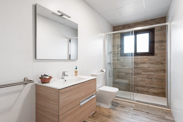 Un baño moderno con tocador de madera, cabina de ducha de vidrio y un inodoro blanco.