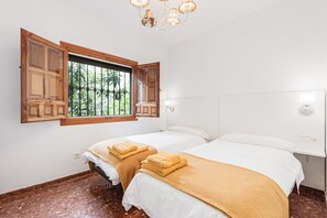 A room with two beds, a window with wooden shutters, a chandelier, and a white wall. - Rural Holiday Home 'Finca Llano de Fe' with Wi-Fi, Garden and Terrace (Málaga)