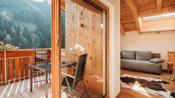 A wooden deck with a glass door leading to a room with a sofa and a cowhide rug. - Apartment 'Bawiglbach Grosskarneid' with Mountain View, Shared Terrace and Wi-Fi (Lüsen)