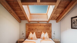 A room with a skylight, wooden beams, a bed with patterned bedding, and bedside tables. - Apartment 'Bawiglbach Grosskarneid' with Mountain View, Shared Terrace and Wi-Fi (Lüsen)