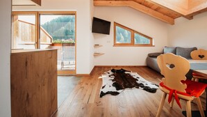 A room with wooden flooring, a cowhide rug, a television, and a dining area with a chair and table. - Apartment 'Bawiglbach Grosskarneid' with Mountain View, Shared Terrace and Wi-Fi (Lüsen)