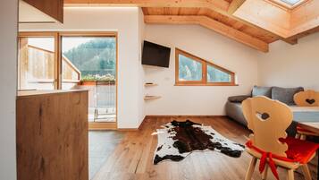 Ein Zimmer mit Holzboden, einem Kuhfellteppich, einem Fernseher und einem Essbereich mit Stuhl und Tisch.