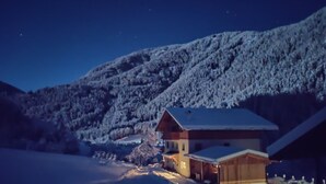 A snow-covered mountain landscape at night with a wooden cabin featuring a porch and a garage. - Apartment 'Bawiglbach Grosskarneid' with Mountain View, Shared Terrace and Wi-Fi (Lüsen)