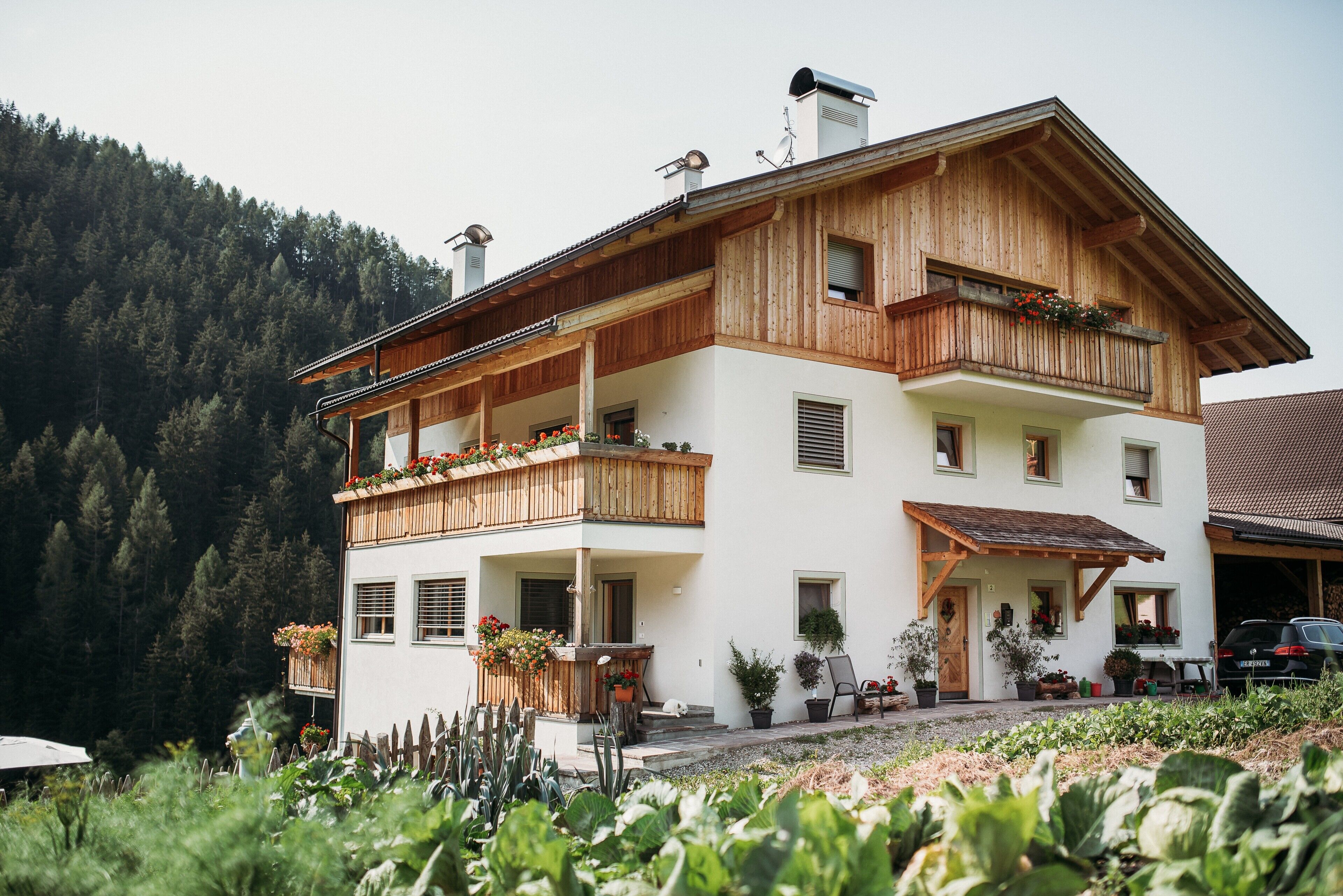 A two-story building with wooden balconies, potted plants, and a view of a forested hillside.