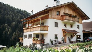 A two-story building with wooden balconies, potted plants, and a view of a forested hillside. - Holiday Apartment “Lahnbach Großkarneid” in Beautiful Scenery with Mountain View (Lüsen)