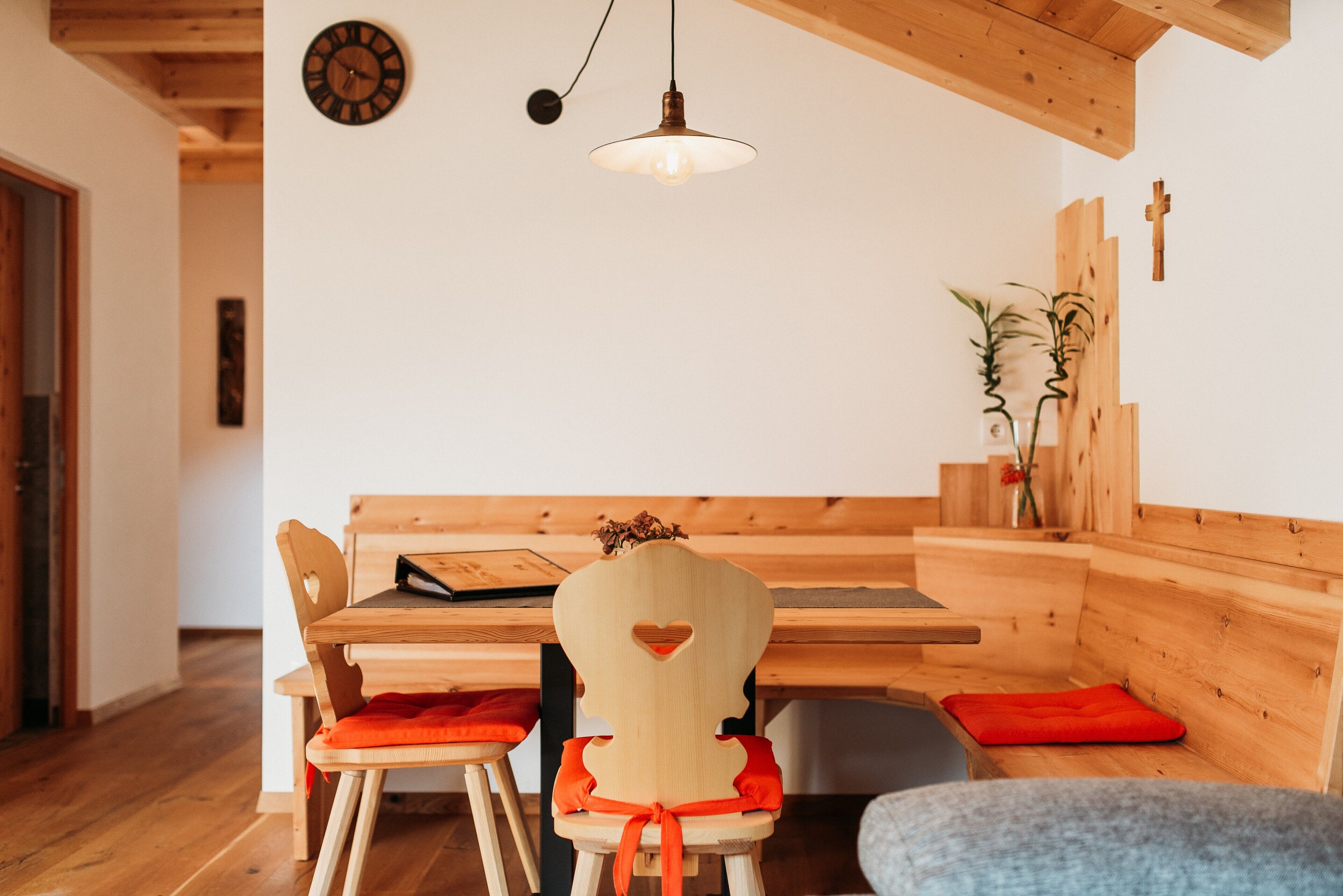 A wooden dining area with a bench and chairs, a hanging light fixture, and a wall clock.