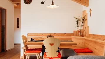 A wooden dining area with a bench and chairs, a hanging light fixture, and a wall clock.