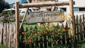 A wooden sign with 'Grobkarnader Hof' written on it, a wooden fence, and a building with balconies and flower boxes. - Holiday Apartment “Lahnbach Großkarneid” in Beautiful Scenery with Mountain View (Lüsen)