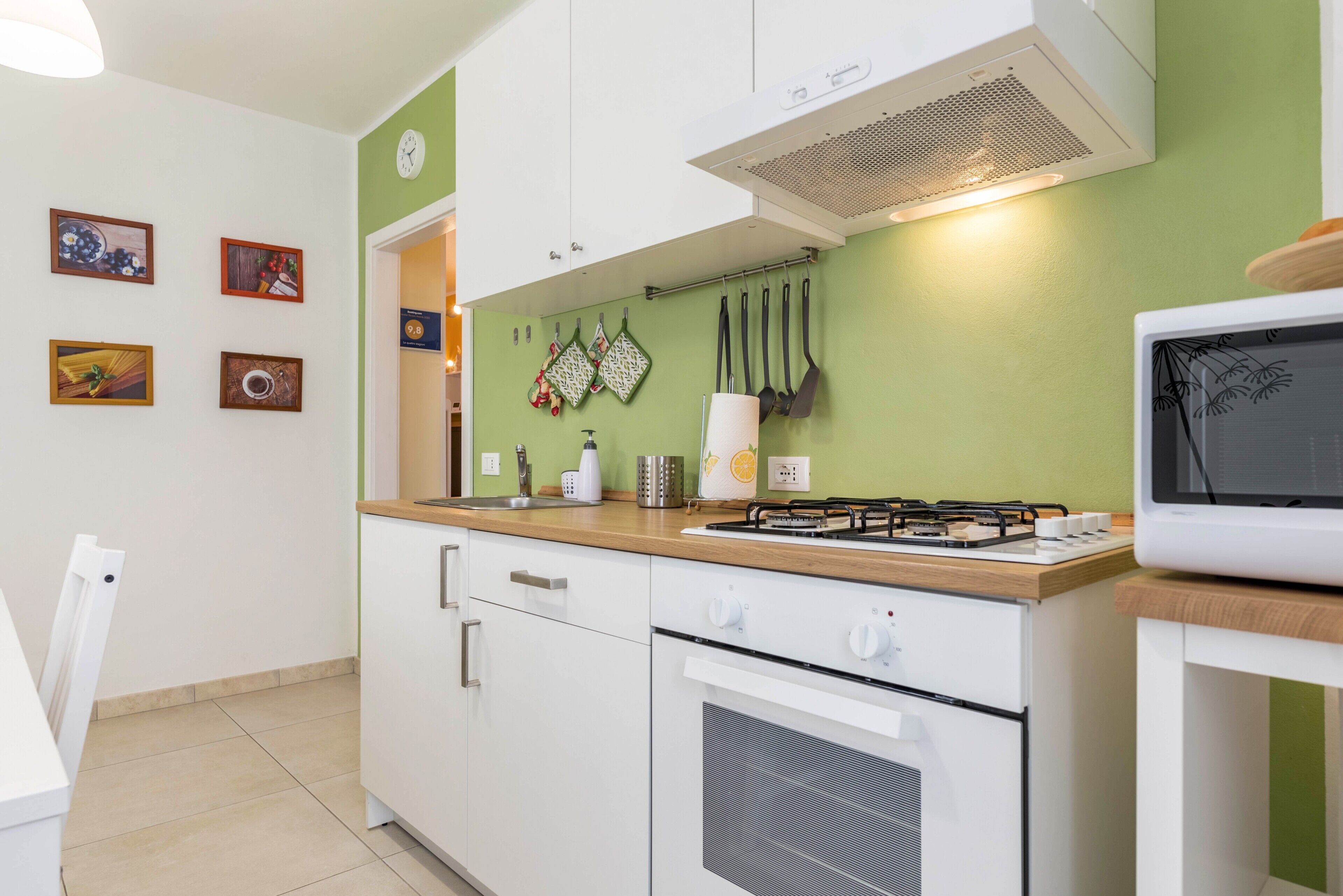 Una cucina con mobili bianchi, un fornello, un forno a microonde e una parete verde.