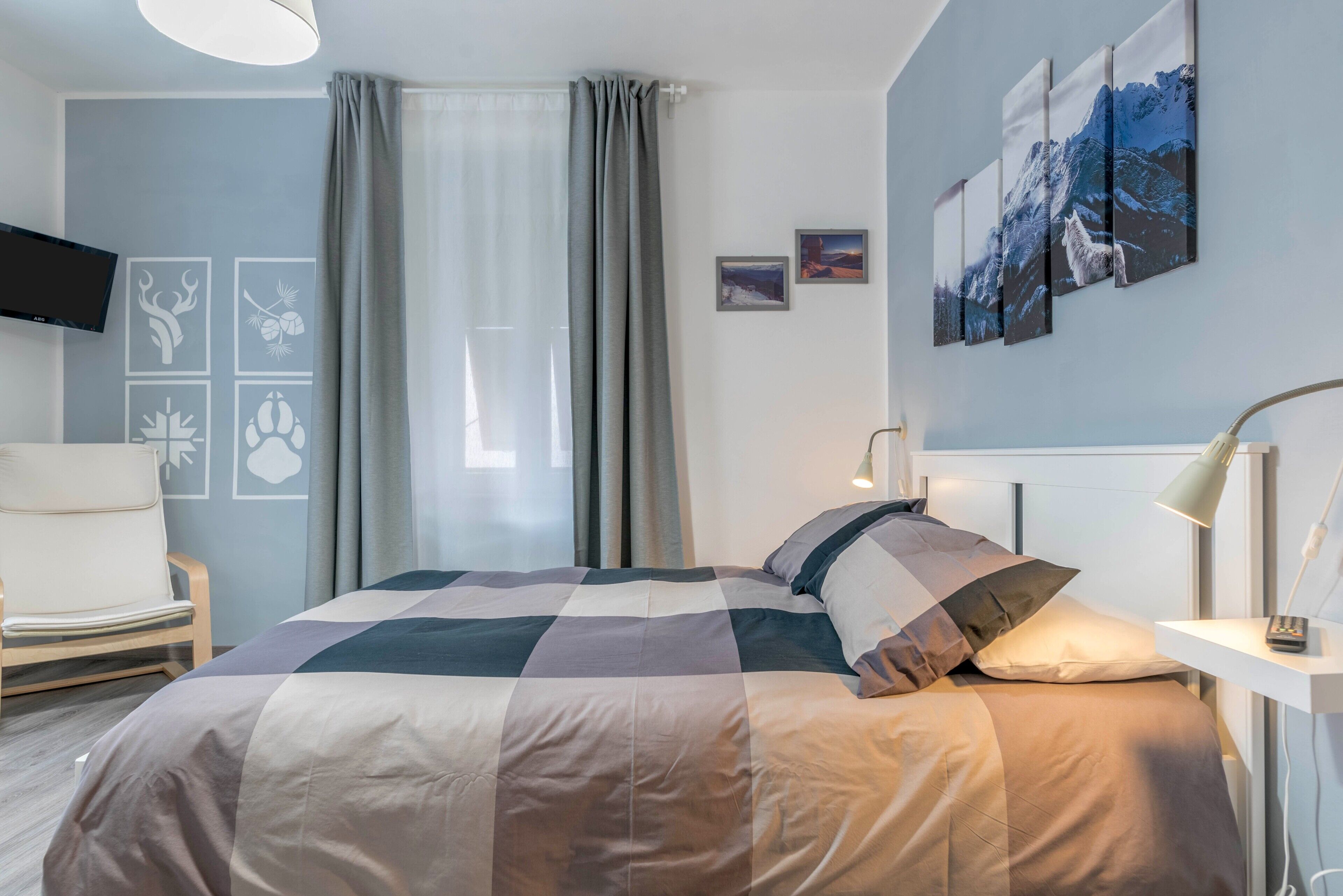Una camera da letto con un letto, una sedia, una televisione e opere d'arte alle pareti.