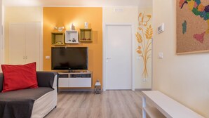 Un salon avec un canapé, un téléviseur, un petit meuble et une porte.