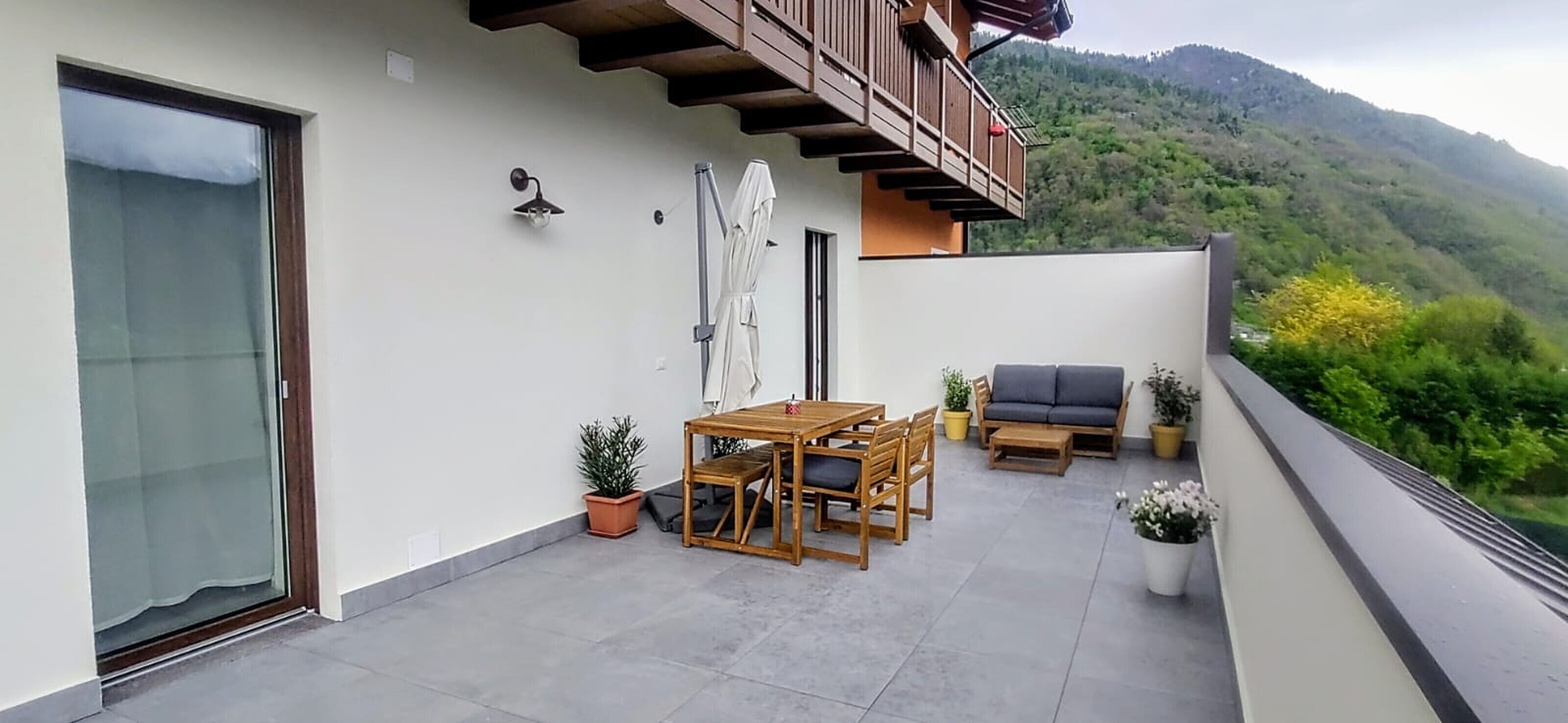 Ein Balkon mit Tisch, Stühlen, einer Couch, Topfpflanzen und Blick auf eine gebirgige Landschaft.