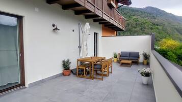 Ein Balkon mit Tisch, Stühlen, einer Couch, Topfpflanzen und Blick auf eine gebirgige Landschaft.