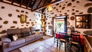Una habitación acogedora con pared de piedra, techo de madera, un sofá, una mesa de comedor con sillas y una pequeña cocina.