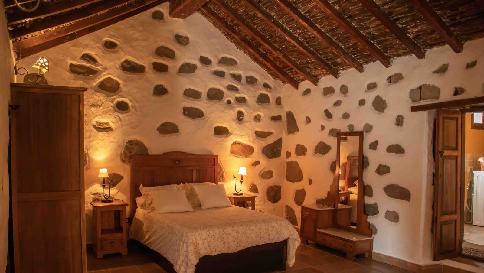 A cozy bedroom with a stone wall, wooden bed frame, and bedside lamps.