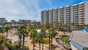 A hotel with multiple floors, a pool area with palm trees, and a view of the city skyline. - 🌴Beach Nearby+ Lagoon Pool -Palms 1503☀️ Pool Views (Destin)