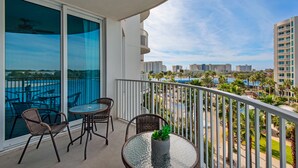 A balcony with a glass door, two wicker chairs, a small table, and a potted plant. - 🌴Beach Nearby+ Lagoon Pool -Palms 1503☀️ Pool Views (Destin)