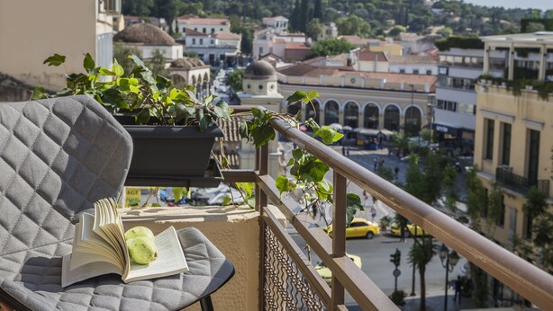 A balcony with a cushioned chair, a book, and a potted plant. - Royalty Hotel Athens (Athens)