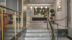 A hotel lobby with marble flooring, a reception desk, a staircase with golden railings, and a red rope barrier. - Royalty Hotel Athens (Athens)