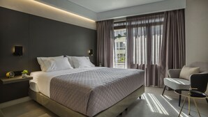 A modern bedroom with a large bed, bedside tables, a chair, and a view of the outdoors through large windows. - Royalty Hotel Athens (Athens)