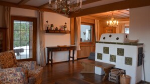 Un salón acogedor con un sofá de madera, una mesa de centro y una chimenea con azulejos decorativos. En el centro, una mesa de madera y un banco, y un candelabro cuelga del techo.