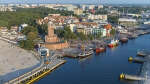 A coastal cityscape with a prominent historic tower, a bustling harbor with boats, and a promenade along the waterfront. - Hotel Hanseatic  - adults only (Kolobrzeg)