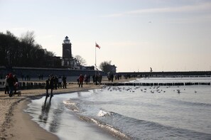 Une plage où l’on voit des gens se promener, un phare et un drapeau.