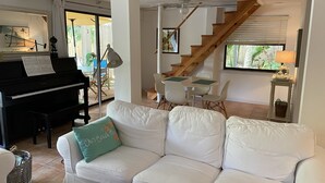A living room with a piano, a white sofa with a cushion, a dining table with chairs, and a wooden staircase. - Enjoy our Private Beach Access! (Vero Beach)