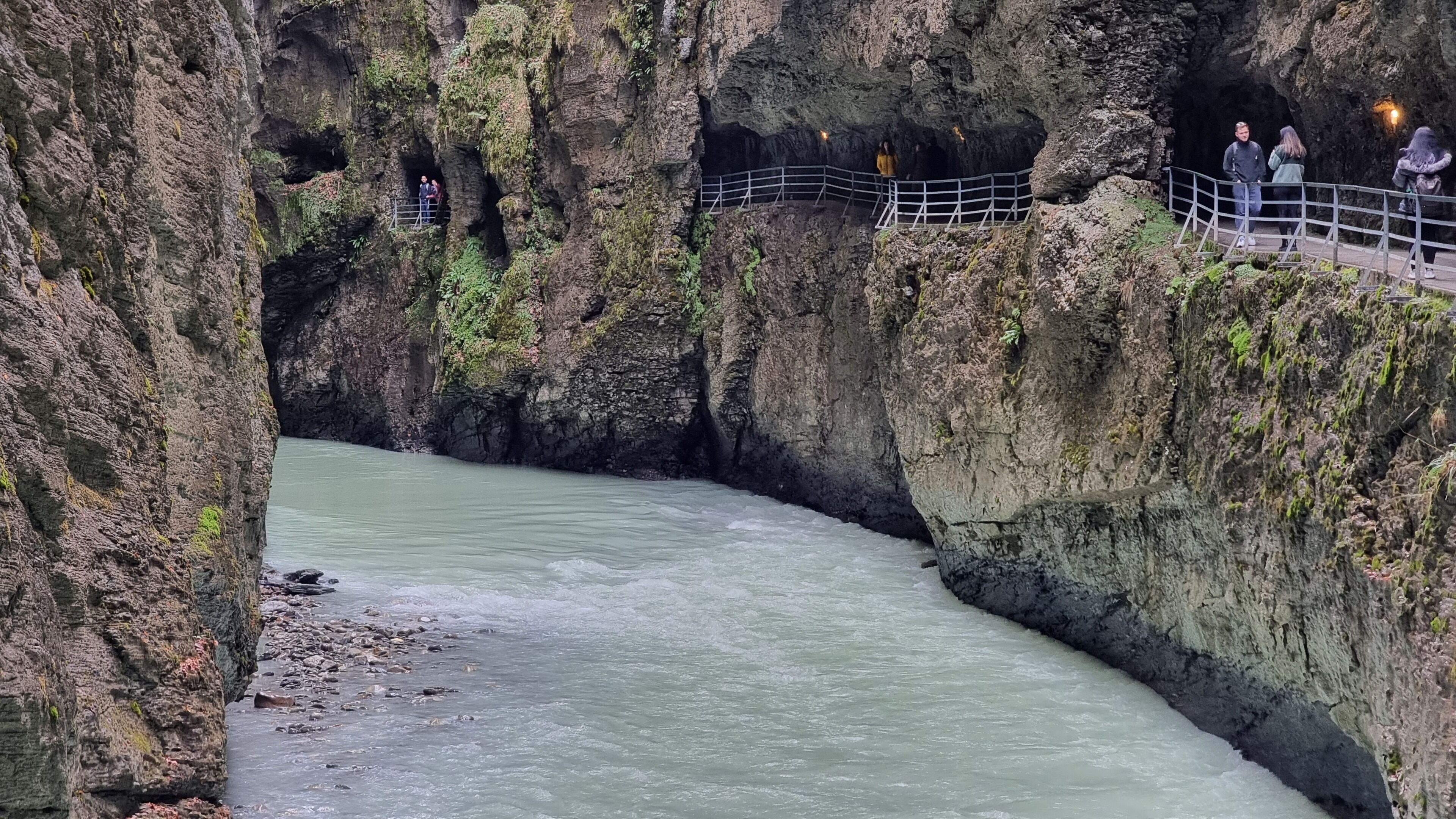 Een rivier die door een rotsachtig ravijn stroomt, met een uitkijkplatform en een leuning.