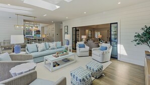 A spacious living room with a sofa, armchairs, ottomans, and a coffee table. There is a dining area with chairs and a table in the background.