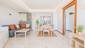 Un salon moderne avec un canapé, une table basse, une table à manger et des chaises. On aperçoit une cuisine au fond.