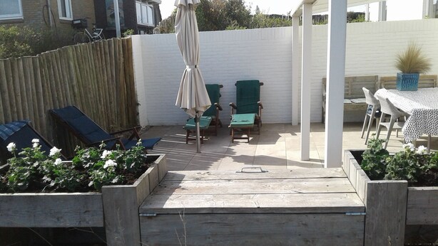 Ein Patio mit Holzdeck, grünen Stühlen, einem Tisch und einem weißen Zaun.