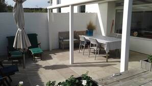 Eine Terrassenfläche mit Tisch, Stühlen und einer Bank, sowie einem Sonnenschirm.