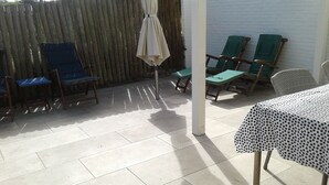 Ein Terrassenbereich mit Fliesenboden, einem Tisch mit bunt gepunktetem Tuch und mehreren Stühlen.