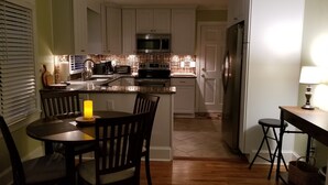 Una cocina moderna con armarios blancos, un refrigerador de acero inoxidable y un microondas. Hay un comedor con una mesa y sillas.