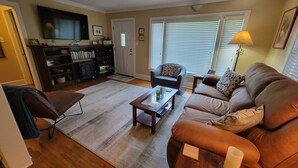 Una sala de estar con un sofá de cuero marrón, una mesa de centro de vidrio, un mueble de centro de madera oscura y un televisor montado en la pared.