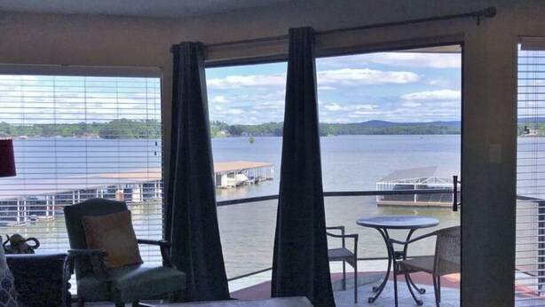 Parveke, josta avautuu näkymä järvelle ja laiturille, ja jossa on tuoli, pöytä ja lamppu.