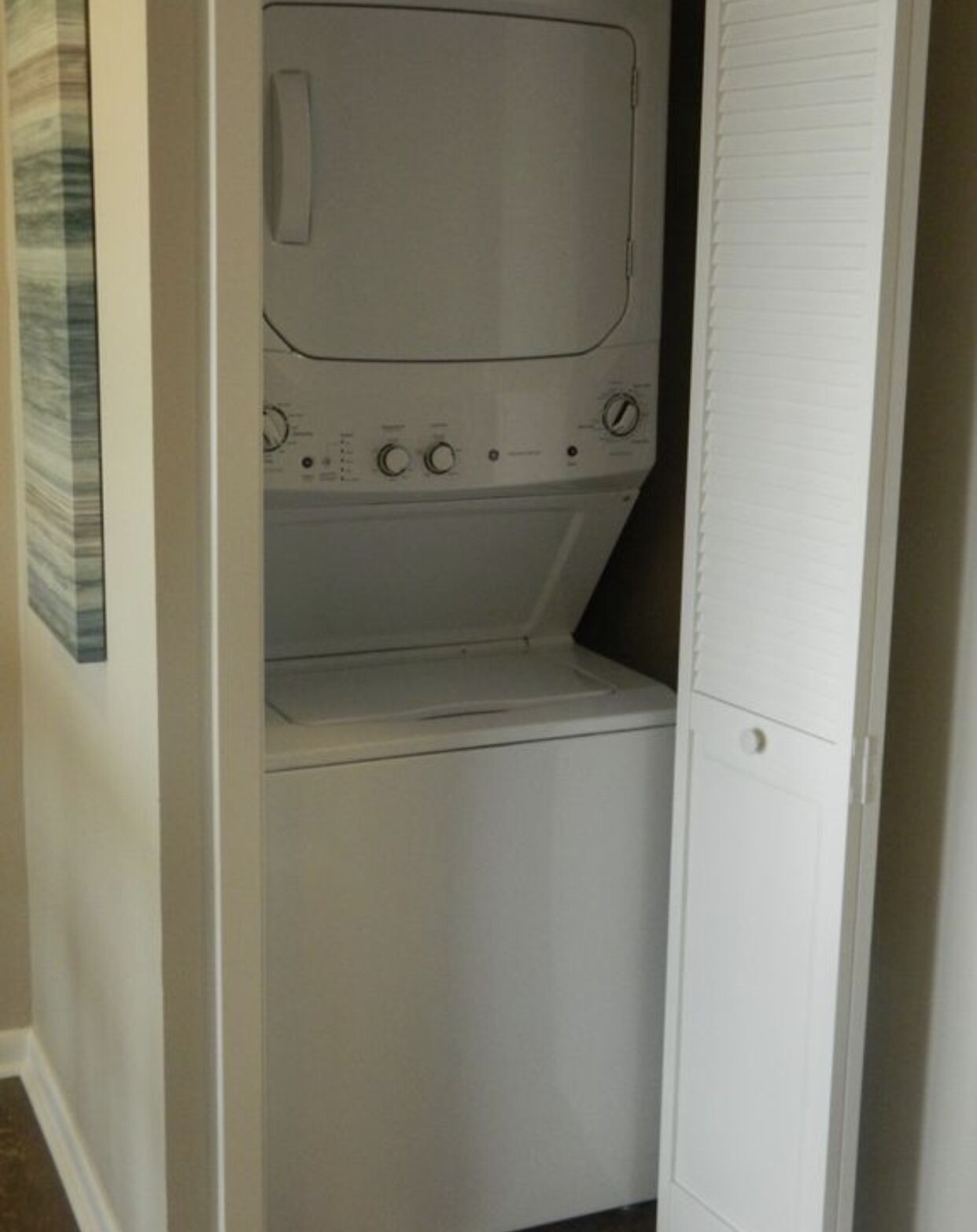 A compact laundry room with a washer and dryer, a small shelf, and a door with a handle.
